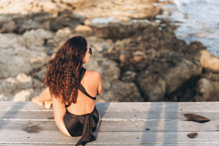 Pretty pan asian woman relaxing on the pier near sea in black swimsuitの写真素材