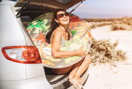 Pretty pan asian brunette with float near car trunk at the seaside beach