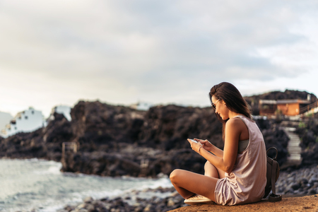 Pretty long hair brunette tourist girl relaxing on the stones near seaの写真素材