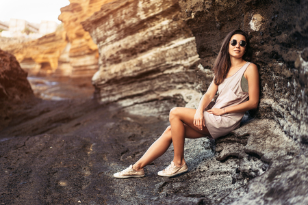 Pretty long hair brunette tourist girl relaxing on the stones near seaの写真素材