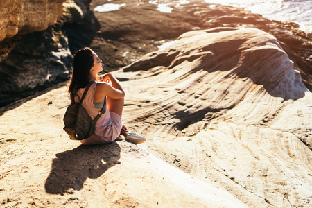 Pretty long hair brunette tourist girl relaxing on the stones near seaの写真素材