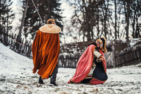 Two ancient warriors in armor with weapons fighting with swords in the snow.の写真素材