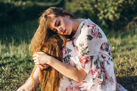 Portrait of a beautiful young woman with curly hair and freckles face. Woman in dress and hat posing in wheat field at sunset and looking at camera.の写真素材