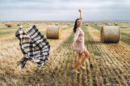 Brunette in linen pants and bare shoulders sitting on a hay bales in warm autumn day. Woman looking...
