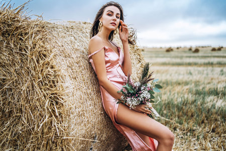 Brunette in linen pants and bare shoulders sitting on a hay bales in warm autumn day. Woman looking...