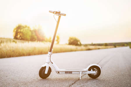 White electric scooter, stand in the middle of the road in the countryside. Content technologies. Sunset time. New movement.の写真素材