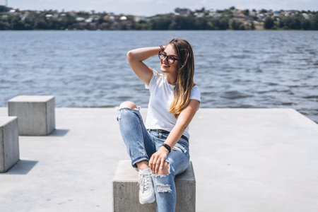 Portrait of a beautiful young woman in stylish glasses. Girl in white tshirt posing on the background of the lake landscape.の写真素材