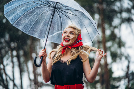 Pretty pin up styled blonde in black vintage swimsuit and hairstyle, with red lips, holding umbrella...