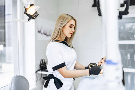 Pretty young female dentist making examination and treatment for young female patient in dental clinicの写真素材
