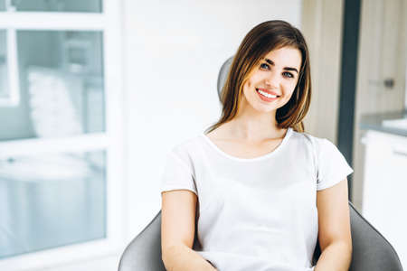 Pretty happy and smiling dental patient sitting in the dental chair at the dental officeの写真素材