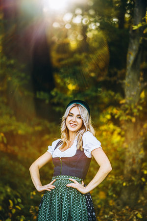 Pretty happy blonde in dirndl, traditional festival dress, holding two mugs of beer outdoors in the...