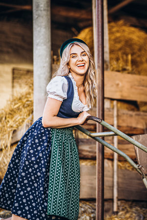 Pretty happy blonde in dirndl, traditional festival dress, holding two mugs of beer outdoors in the forest with blurred background. Oktoberfest, St. Patrickâs day, international beer day concept.の写真素材