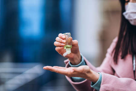 Close up hands of female in medical mask cleaning her hands with sanitizer outdoor in the city to prevent virus deseases. Coronavirus, COVID-19, epidemic, pandemic, quarantine conceptの写真素材