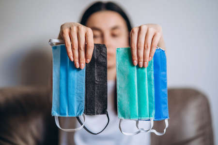 Female at home in quarantine time holding colorful protective medical masks to prevent virus disease, COVID-19, pandemic, epidemic conceptの写真素材