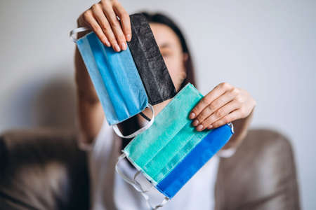 Female at home in quarantine time holding colorful protective medical masks to prevent virus disease, COVID-19, pandemic, epidemic conceptの写真素材