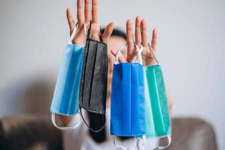 Female at home in quarantine time holding colorful protective medical masks to prevent virus disease, COVID-19, pandemic, epidemic conceptの写真素材