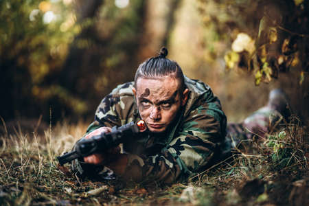 Portrait of a camouflage soldier with rifle and painted face playing airsoft outdoors in the forest. Side view.