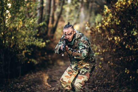 Portrait of a camouflage soldier with rifle and painted face playing airsoft outdoors in the forest. Side view.の写真素材