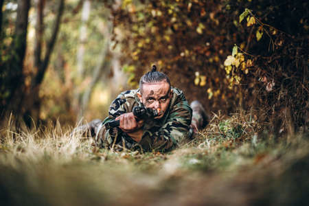 Portrait of a camouflage soldier with rifle and painted face playing airsoft outdoors in the forest. Side view.の写真素材
