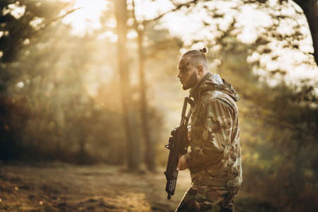 Portrait of a camouflage soldier with rifle and painted face playing airsoft outdoors in the forest. Side view.の写真素材