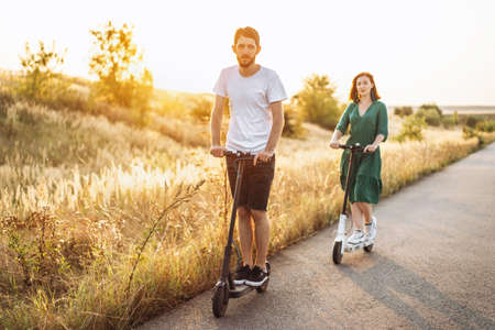 Portrait of young couple at sunset with beautiful natural landscape. Walking on electric scooters in the countryside.の写真素材