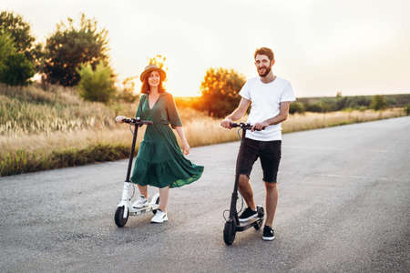 Portrait of young couple at sunset with beautiful natural landscape. Walking on electric scooters in the countryside.の写真素材