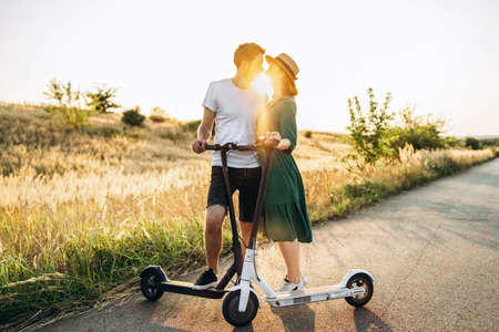 Portrait of young couple at sunset with beautiful natural landscape. Walking on electric scooters in the countryside.の写真素材