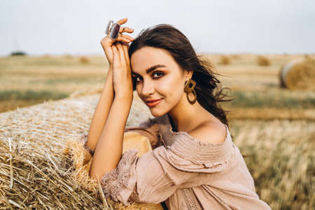 Closeup portrait of beautiful smiling woman with closed eyes. The brunette leaned on a bale of hay. A wheat field on the background.の写真素材