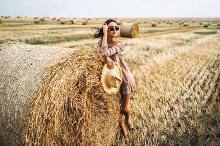 Closeup portrait of beautiful smiling woman with closed eyes. The brunette leaned on a bale of hay. A wheat field on the background.の写真素材