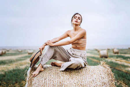 Closeup portrait of beautiful smiling woman with closed eyes. The brunette leaned on a bale of hay. A wheat field on the background.の写真素材