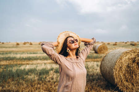 Closeup portrait of beautiful smiling woman with closed eyes. The brunette leaned on a bale of hay. A wheat field on the background.の写真素材