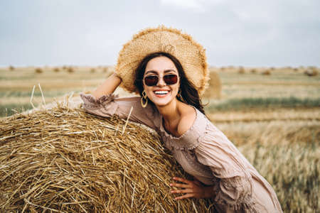 Closeup portrait of beautiful smiling woman with closed eyes. The brunette leaned on a bale of hay. A wheat field on the background.の写真素材