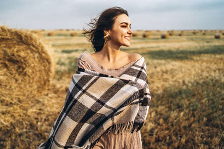 Closeup portrait of beautiful smiling woman with closed eyes. The brunette leaned on a bale of hay. A wheat field on the background.の写真素材