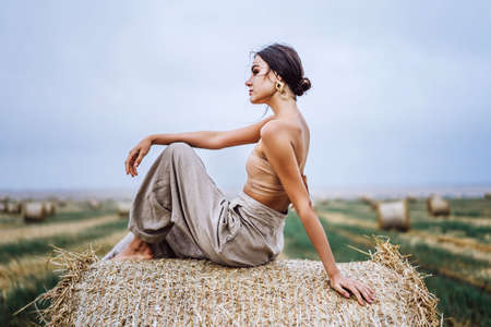 Closeup portrait of beautiful smiling woman with closed eyes. The brunette leaned on a bale of hay. A wheat field on the background.の写真素材