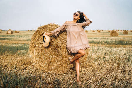 Closeup portrait of beautiful smiling woman with closed eyes. The brunette leaned on a bale of hay. A wheat field on the background.の写真素材