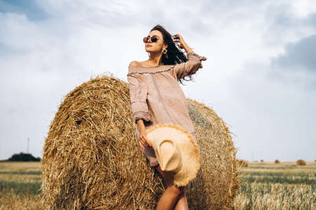 Closeup portrait of beautiful smiling woman with closed eyes. The brunette leaned on a bale of hay. A wheat field on the background.の写真素材