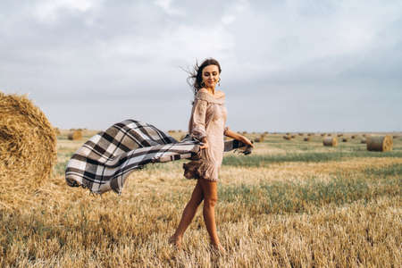 Closeup portrait of beautiful smiling woman with closed eyes. The brunette leaned on a bale of hay. A wheat field on the background.の写真素材