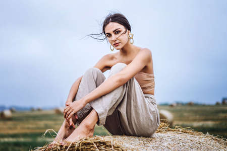 Closeup portrait of beautiful smiling woman with closed eyes. The brunette leaned on a bale of hay. A wheat field on the background.の写真素材