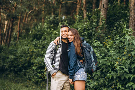 Young couple with backpacks on their backs smiling and walking in the forest, enjoy the walk.の写真素材