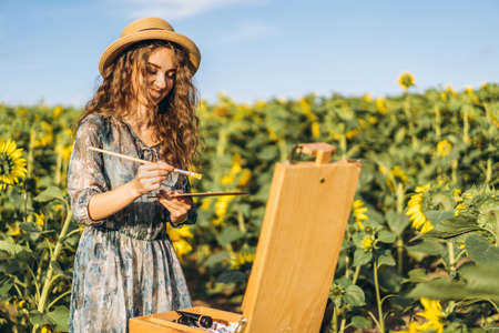Closeup portrait of a beautiful young woman with curly hair. Woman in dress and hat standing in wheat field.の写真素材