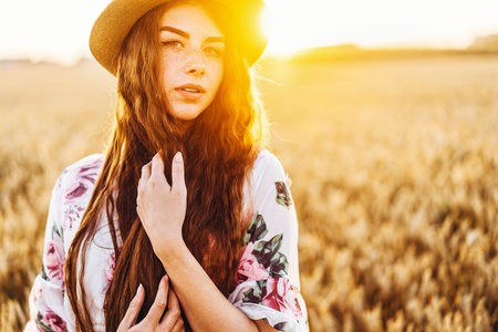 Full length portrait of beautiful woman with long curly hair on currant field background. Girl in a light dress sits on the grass in sunny day.の写真素材