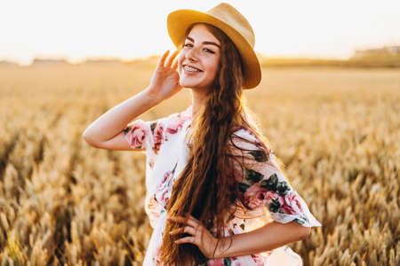 Full length portrait of beautiful woman with long curly hair on currant field background. Girl in a light dress sits on the grass in sunny day.の写真素材