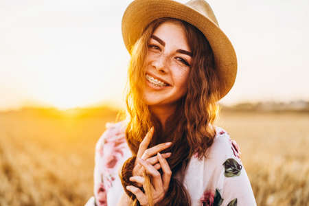 Full length portrait of beautiful woman with long curly hair on currant field background. Girl in a light dress sits on the grass in sunny day.の写真素材