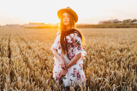 Full length portrait of beautiful woman with long curly hair on currant field background. Girl in a light dress sits on the grass in sunny day.の写真素材
