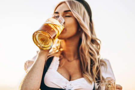 Close-up portrait of pretty happy blonde in dirndl, traditional festival dress, drinking beer outdoors. Oktoberfest, St. Patrickâs day, international beer day concept.の写真素材