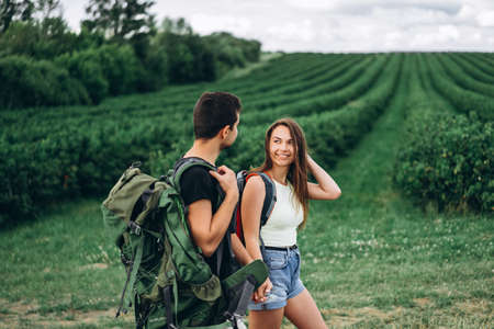 Portrait of happy young couple with backpacks on the field in spring. Man and woman walking in currant plantations.の写真素材