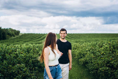 A tender loving couple walking in a field of currant. A smiling woman with long hair leads a man, holding his hand.の写真素材