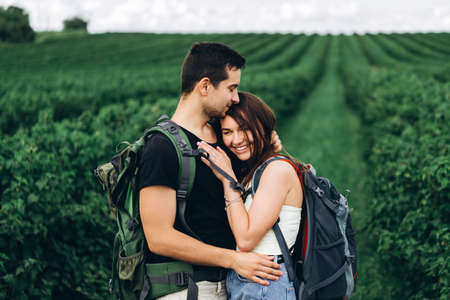 Portrait of happy young couple with backpacks on the field in spring. Man and woman walking in currant plantations.の写真素材