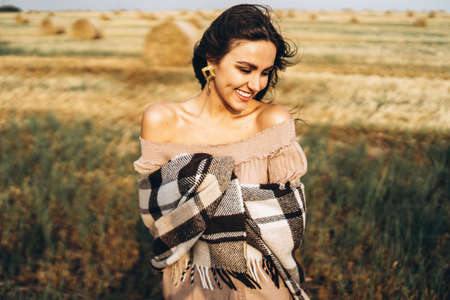 Portrait of a beautiful brunette in a dress and with a warm plaid. Woman enjoying a walk in a wheat field with hay bales.の写真素材