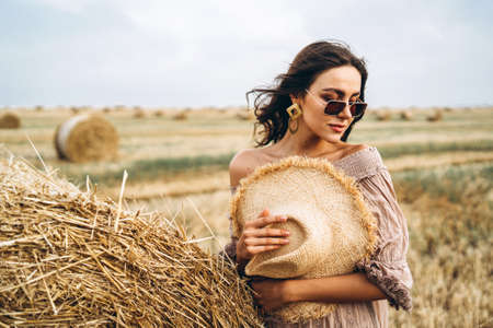 Smiling woman in sunglasses with bare shoulders on a background of wheat field and bales of hay.の写真素材